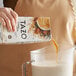 A yellow hand pours Tazo Chai Tea Latte concentrate into a pitcher.