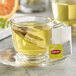 A glass cup of Lipton Green Tea with a tea bag in it, with orange and lemon slices.