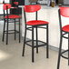 Lancaster Table & Seating Boomerang Series Black Finish Bar Stool with Red Vinyl Seat and Back on a counter in a cocktail bar.