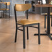 A Lancaster Table & Seating black chair with light brown vinyl seat and back on a table in a restaurant.