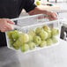 A person holding a Vigor clear polycarbonate food storage box full of green apples.