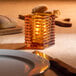 A Hollowick amber glass square candle holder on a table with a lit candle.