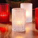 A clear glass Hollowick vertical cylinder candle holder with a lit candle inside.