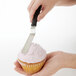 A person's hand icing a cupcake with an OXO Good Grips offset baking spatula.