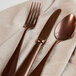 A Sola Baguette vintage copper stainless steel table knife on a white cloth with a fork and spoon.