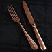 A Sola Baguette vintage copper stainless steel table knife on a black surface with a fork.