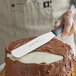 A hand with a Dexter-Russell V-Lo baking/icing spatula with a black rubber handle cutting a cake.