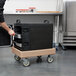 A man using a Cambro Camdolly to transport a large black box.