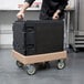A person pushing a Cambro Camdolly with a black box on it.