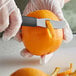 A hand using a Mercer Culinary stainless steel citrus peeler to peel an orange.