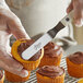 A person using an Ateco offset spatula to spread chocolate frosting on a cupcake.