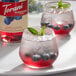 A glass of blueberry and mint cocktail next to a bottle of Torani Puremade Blueberry Flavoring Syrup.