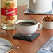 A close up of a Torani Puremade Almond Flavoring Syrup bottle on a table with a cup of coffee.