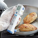 A person using a Comark digital infrared thermometer to check the temperature of food in a frying pan.