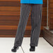 A person wearing Uncommon Chef chalk stripe chef pants with a black and white striped pattern.