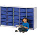 A young girl sitting next to a blue and white Rainbow Accents storage unit reading a book.