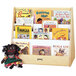 A wooden shelf with books and a doll on a Jonti-Craft double-sided book stand.