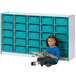 A young girl sitting on the floor next to a Rainbow Accents teal storage unit filled with blue bins reading a book.