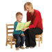 A woman reading a book to a child sitting on a Jonti-Craft Baltic Birch Instructor's Ladderback Chair.