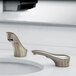 A Bobrick brushed nickel automatic faucet on a bathroom counter with two faucets.