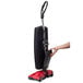 A person holding a red Sanitaire QUICKBOOST cordless upright vacuum cleaner.