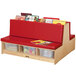 A Jonti-Craft Read-a-Round double-sided wood bench with red cushions and books on it.