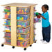 A child standing next to a Jonti-Craft mobile wood tub storage tower filled with plastic containers of toys.