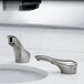 A Bobrick polished nickel counter-mounted automatic liquid soap dispenser above a white bathroom sink with two faucets.