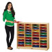 A woman in a green sweater standing next to a Jonti-Craft mobile wood classroom mailbox organizer with colorful papers on the shelves.