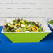 A green Keywest melamine bowl filled with salad on a white table.
