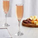 Two Acopa tall flute glasses of champagne next to a plate of cheese and crackers on a table.