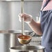 A person using a Vollrath stainless steel ladle to pour soup into a pot.