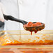 A person using a Vollrath High Heat Perforated Nylon Spoodle to serve red sauce.