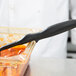 A chef uses a Vollrath High Heat Perforated Spoodle with a black handle to serve food from a glass container.