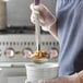A person using a Vollrath Jacob's Pride ladle with a white bowl of food.