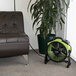An XPOWER green and black utility fan next to a plant on a leather chair.