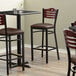 A Lancaster Table & Seating Bistro Bar Stool with a black vinyl seat and mahogany back.
