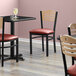 A Lancaster Table & Seating bistro chair with a black finish and burgundy vinyl seat and natural wood back.