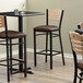 A set of three Lancaster Table & Seating black bistro bar stools with dark brown vinyl seats.