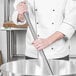 A chef using a Thunder Group stainless steel piano whisk to stir a large pan.