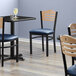 A Lancaster Table & Seating black bistro chair with navy vinyl seat and natural wood back.