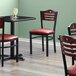 A Lancaster Table & Seating black bistro chair with mahogany wood back and burgundy vinyl seat.