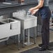 A woman standing at a Regency stainless steel underbar sink putting a glass in.