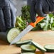 A person in black gloves using a Victorinox Swiss Classic orange handle paring knife to cut a cucumber.