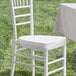A white chair with a white cushion sitting next to a table in the grass.