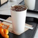 A white Choice paper cold cup filled with a brown liquid on a tray with snacks.