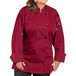 A woman wearing a Uncommon Chef burgundy long sleeve chef coat with 10 buttons.