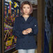 A woman wearing a navy blue Uncommon Chef long sleeve chef coat with 10 buttons.