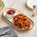 An Acopa vanilla bean stoneware platter with fried onion rings and ketchup on it.