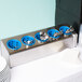 A Steril-Sil stainless steel countertop organizer with silverware in blue containers.
